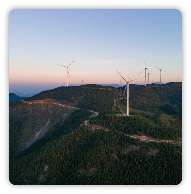 Wind farm with white fans on a hillside with view of the ocean and sunset