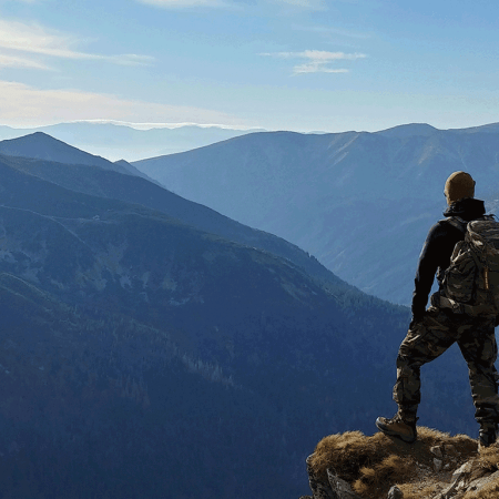 Hiker on top of a mountain looking out at mountain ranges set against blue sky and clouds