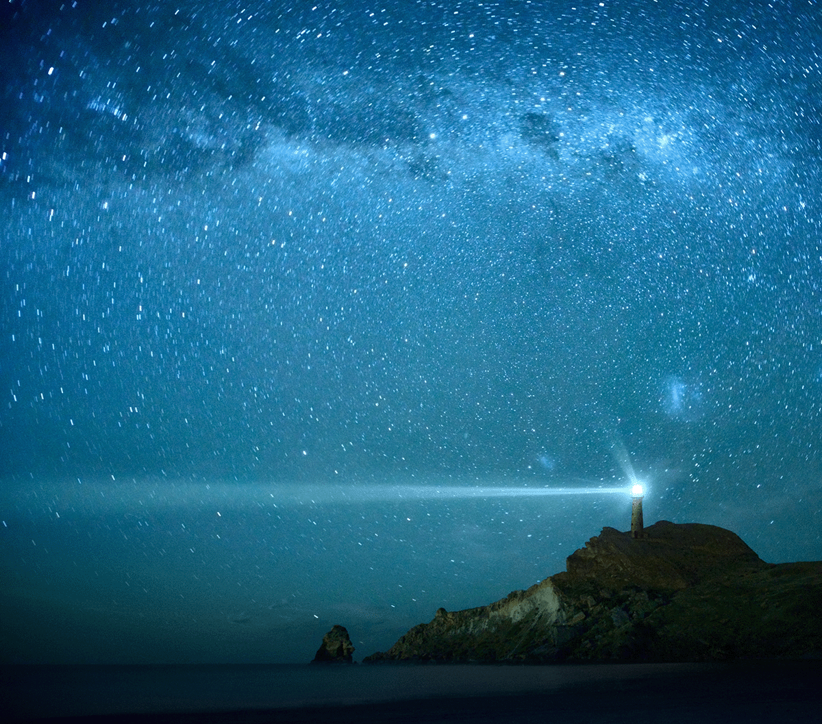 Lighthouse on hilltop set against the night sky filled with countless stars