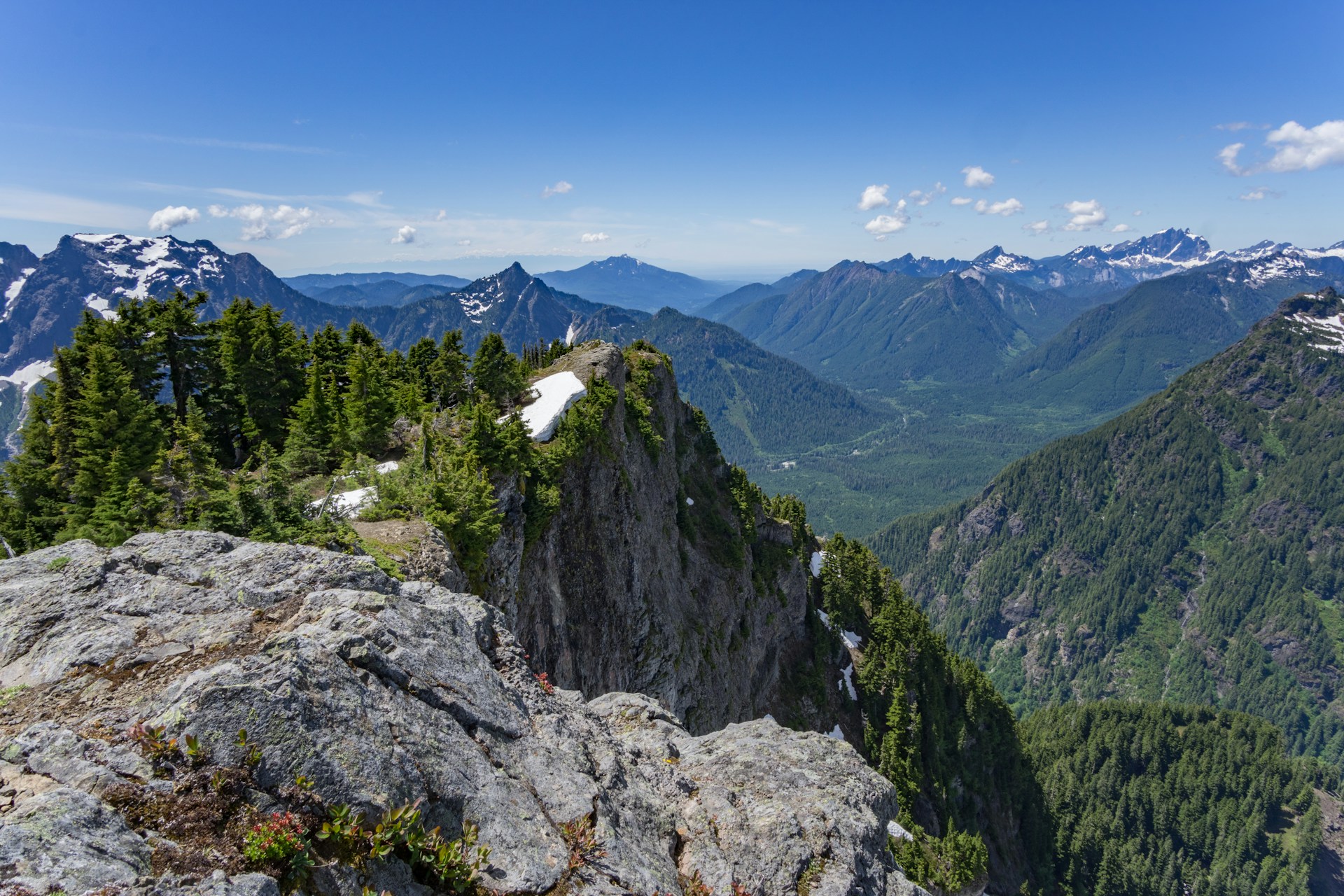 A series of mountain ranges covered in green trees with blue skies and soft clouds