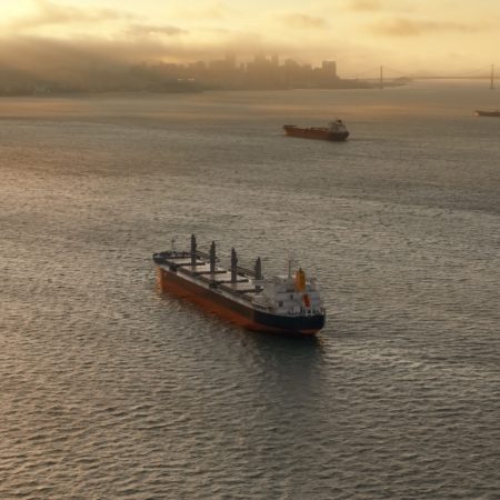 Aerial view of large cargo ships approaching San Francisco Bay at sunset in California, USA.