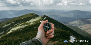 person holding compass with mountains in background