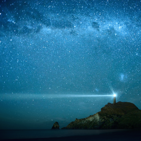 Lighthouse on hilltop set against the night sky filled with countless stars