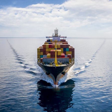 Aerial front view of a loaded container cargo vessel traveling over calm ocean